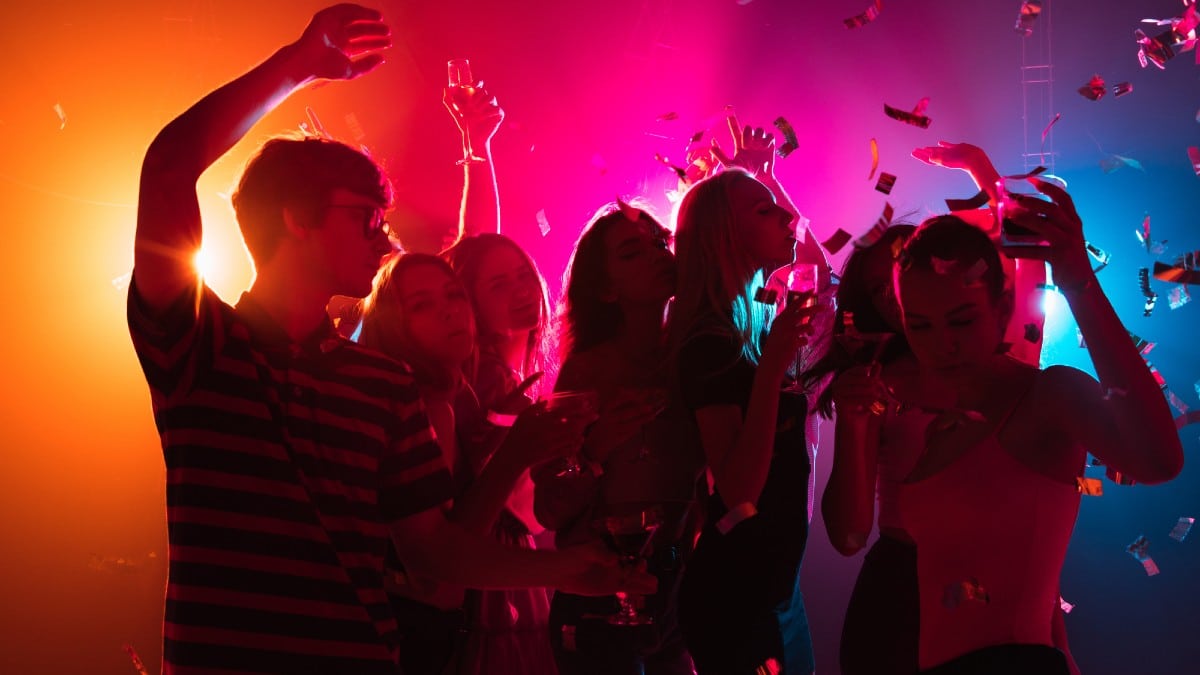 A crowd of people in silhouette raises their hands on dancefloor