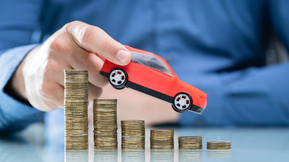 Businesswoman's Hand Driving Blue Car On Declining Stacked Coins