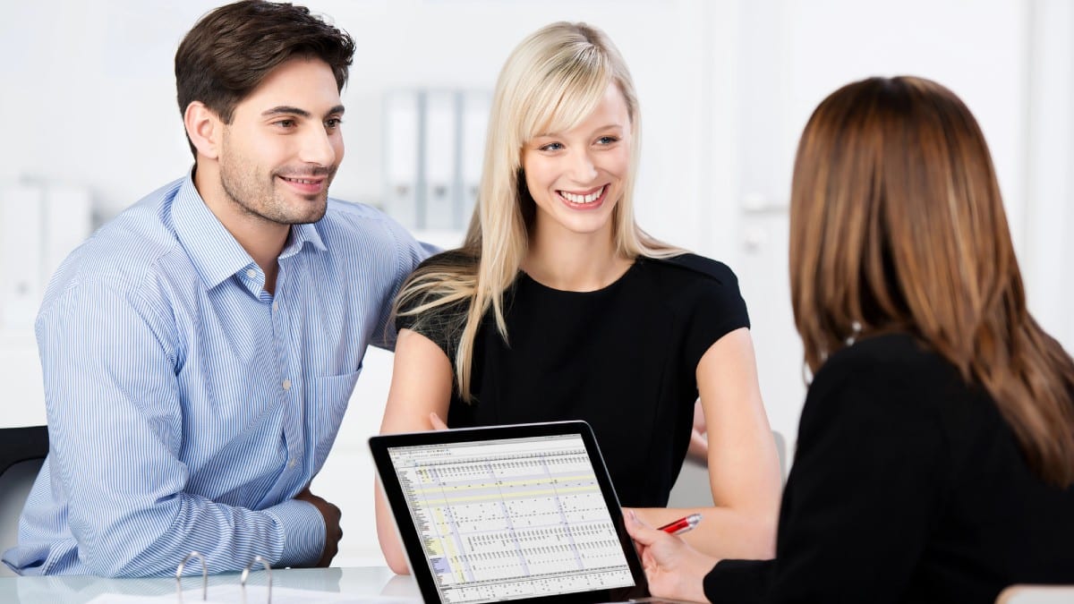 Couple Smiling While Looking At Financial Advisor At Desk