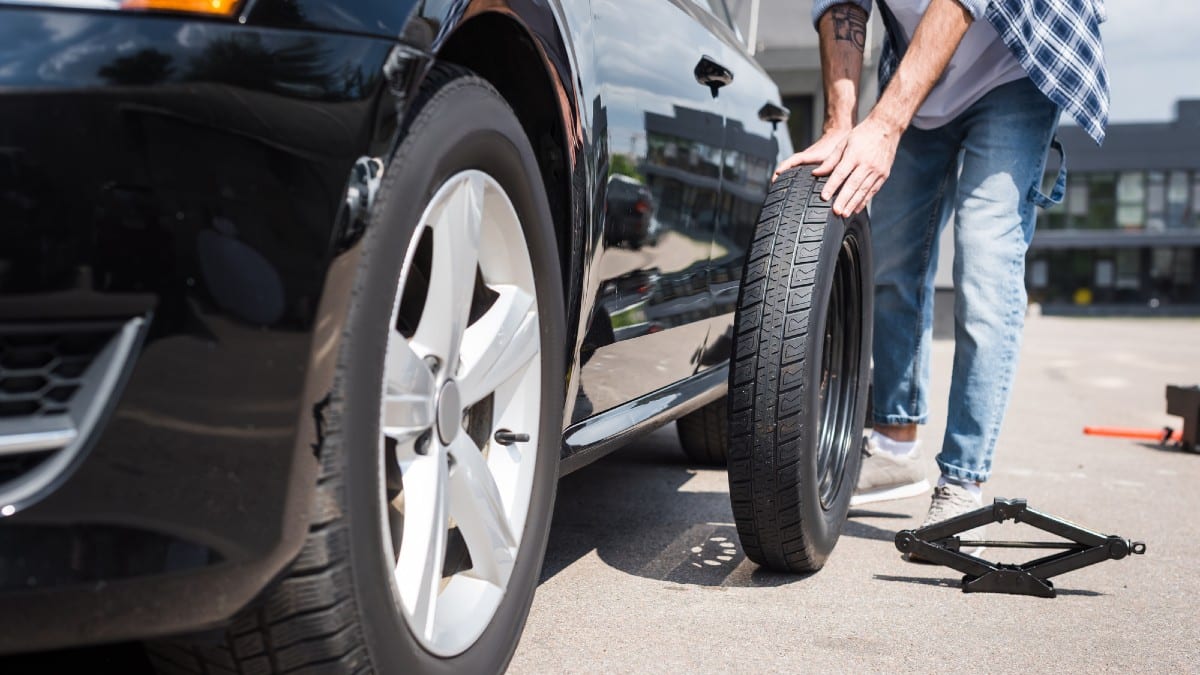 Cropped view of man rolling new tire and fixing broken auto