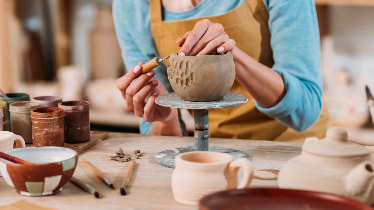 Cropped-view-of-potter-in-apron-decorating-ceramic-bowl-in-workshop