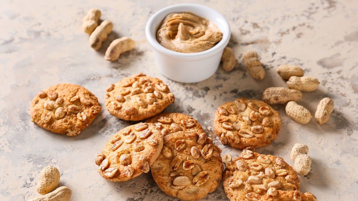 Tasty peanut cookies and butter on beige background