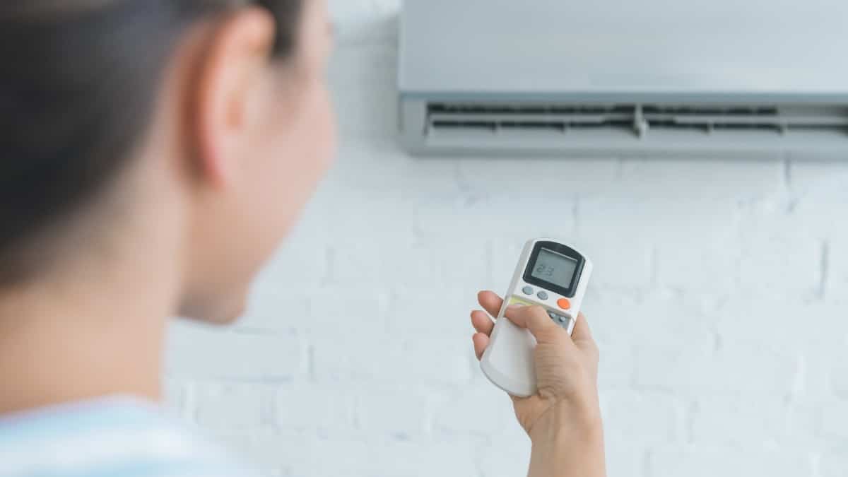 Woman with remote control turning on air conditioner.