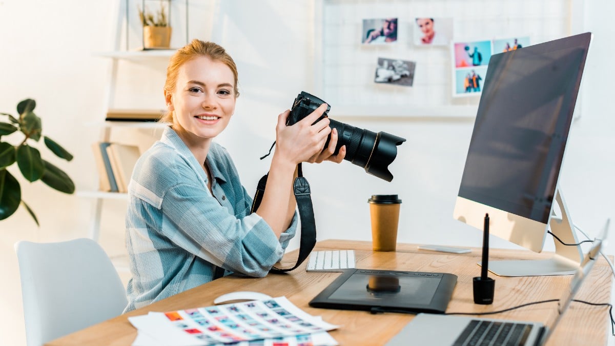 Beautiful young female photographer smiling at camera while working in office