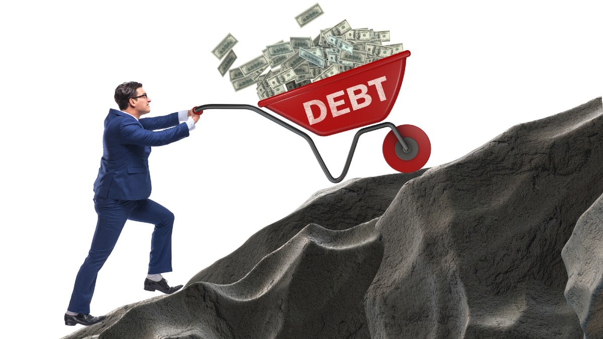Businessman pushing wheelbarrow uphill in debt loan concept