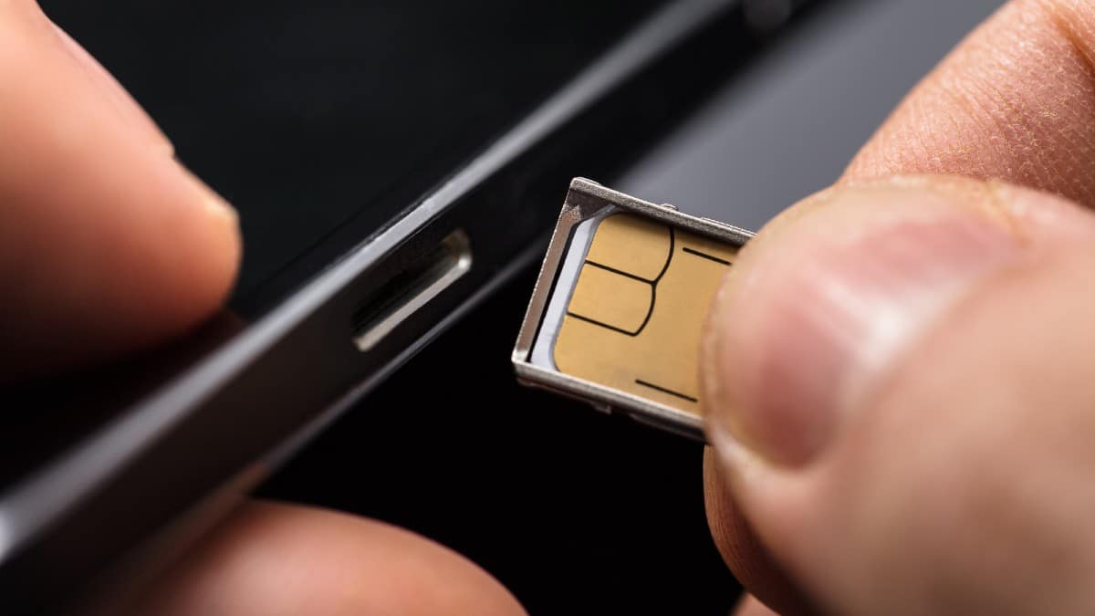 Close-up Of A Person Inserting A Sim Card Into The Back Of A Mobile