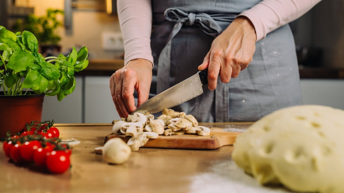 Close up of woman cutting mushroom using knife in home kitchen