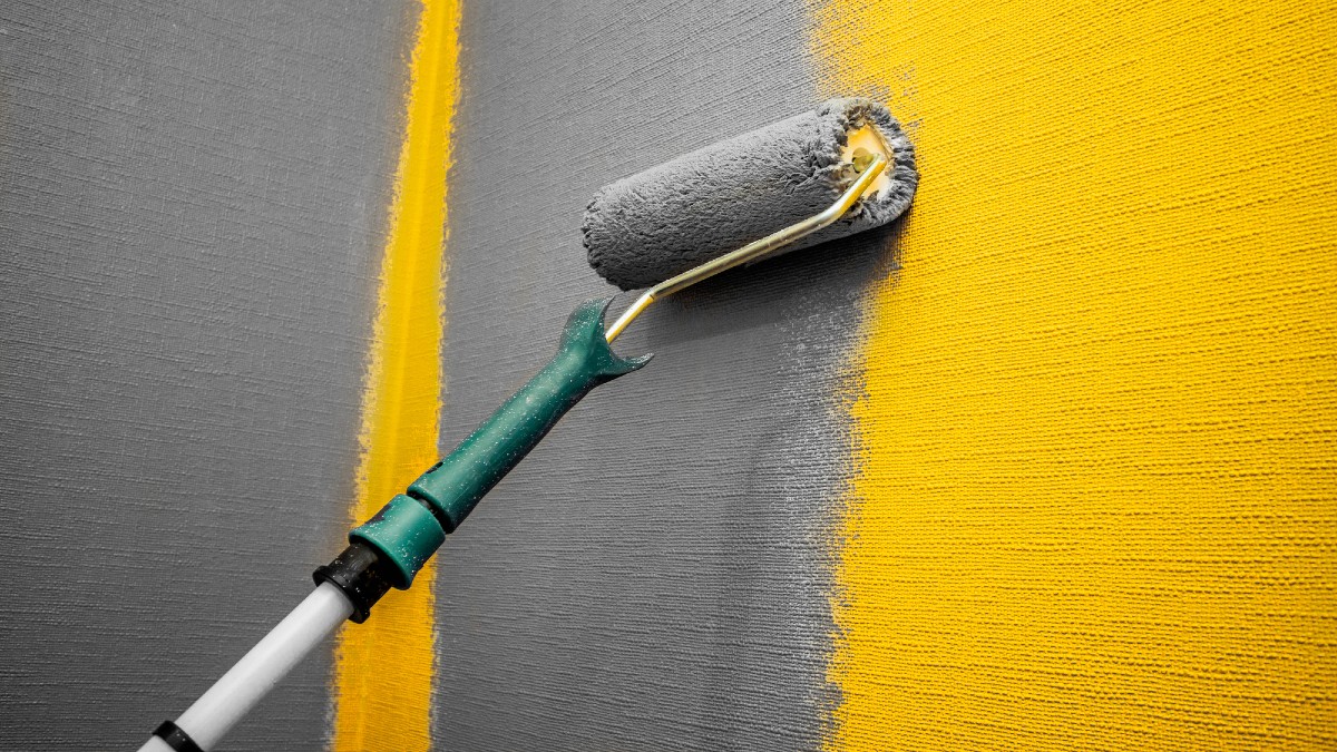 Close up roller with gray paint for painting walls. Repairs. Yellow wall.