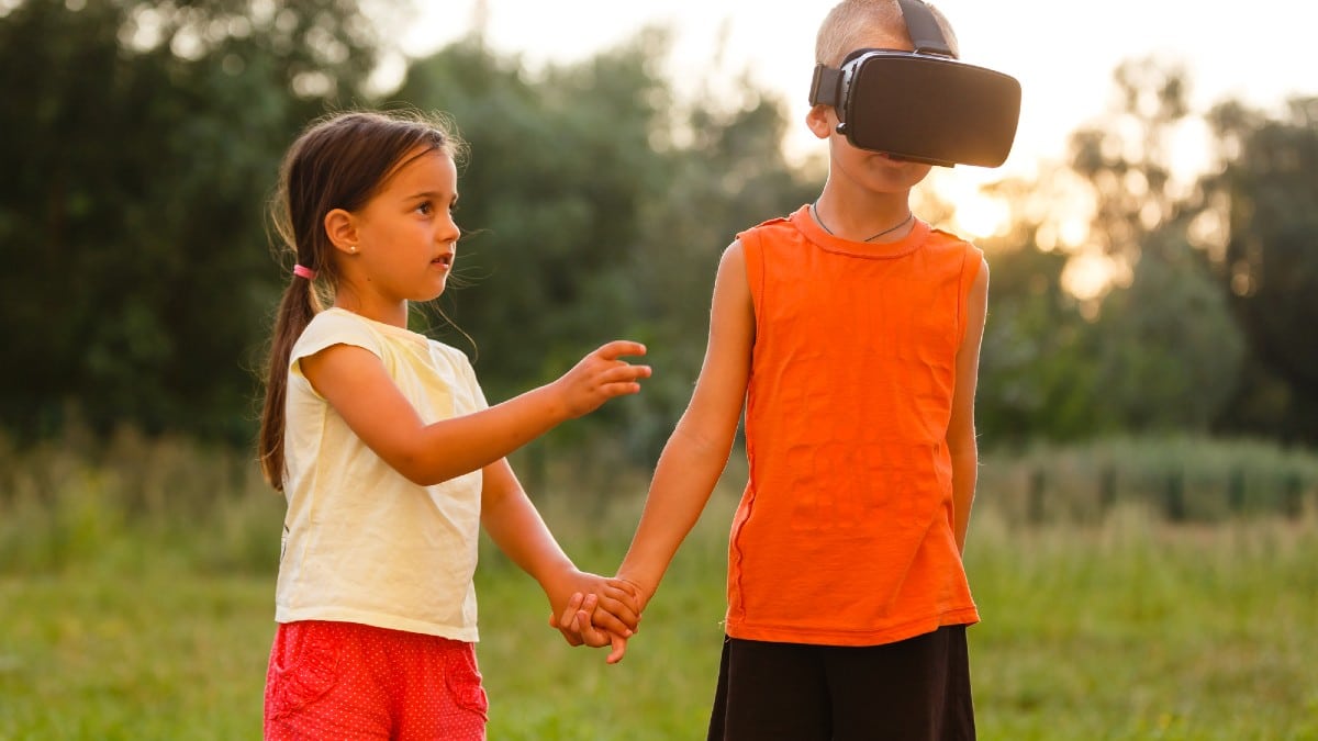 Little girl with brother in virtual reality headsets playing together in park