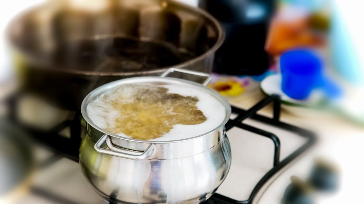 Metal pot with pasta and boiling water on the kitchen burner