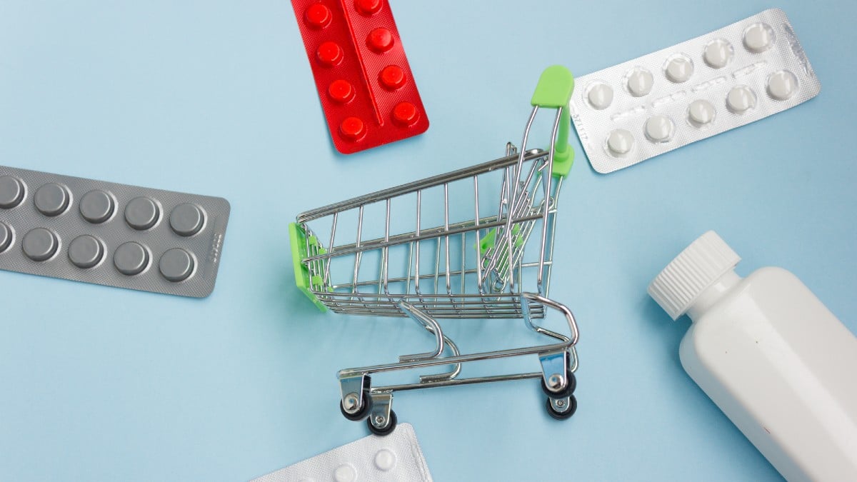 Shopping cart loaded with pills on blue background.