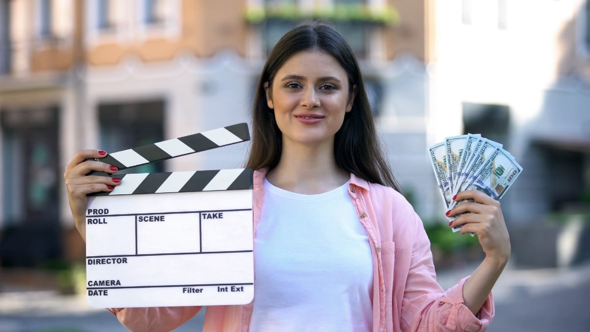 Smiling woman holding clapperboard and bunch of dollars,