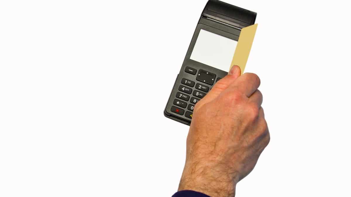 The hand holds a credit card on the payment terminal.