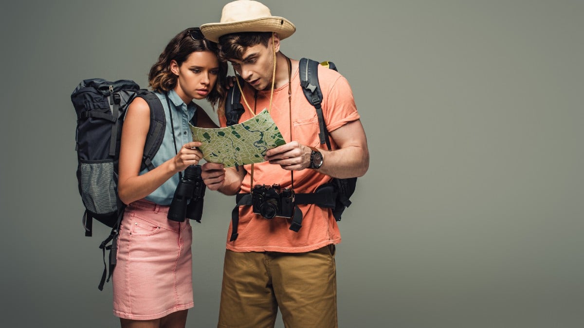 Two young tourists looking at geographic map on grey background