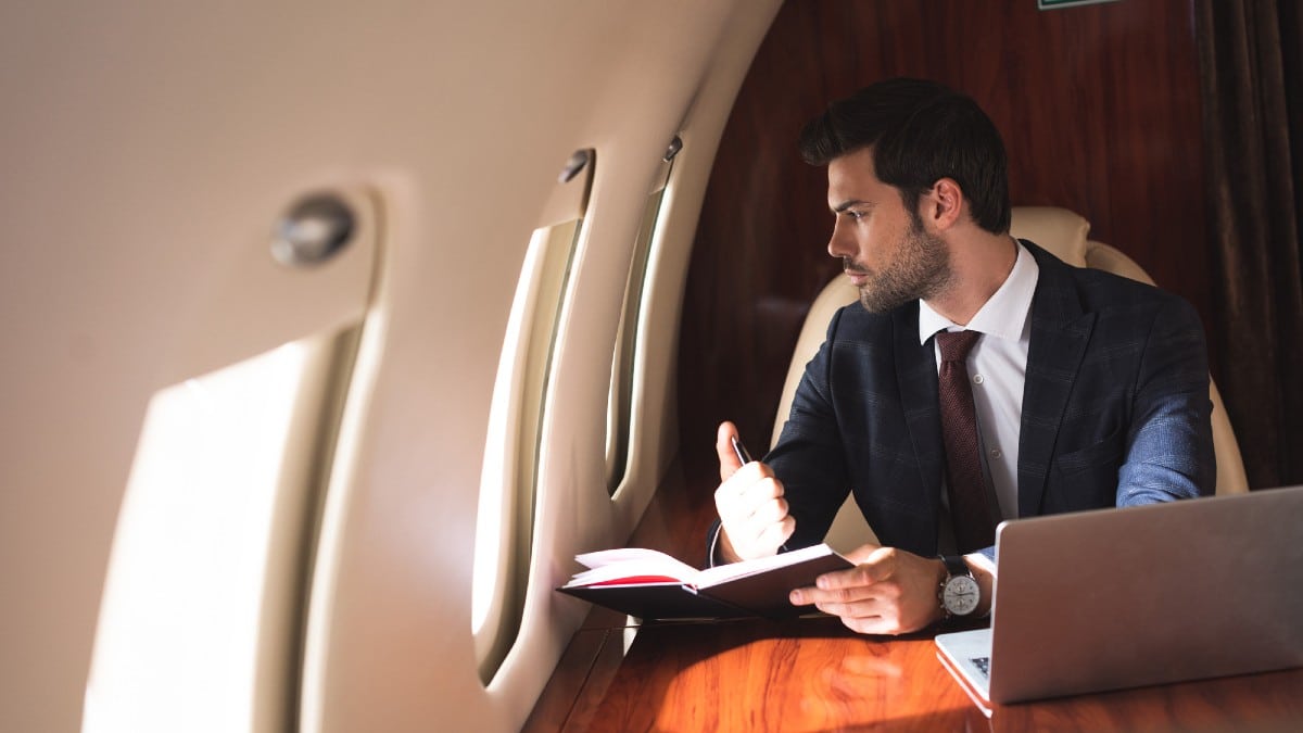 Young businessman working with notebook and laptop in plane