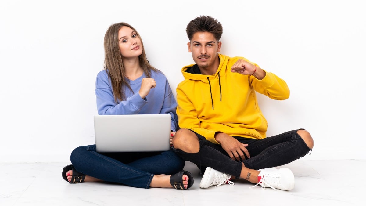 Young couple with a laptop sitting on the floor isolated on white